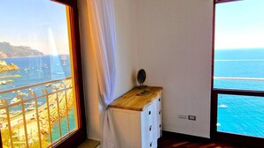 Ein Zimmer mit großem Fenster und Blick auf eine Küstenlandschaft, Boote und freien Meerblick.