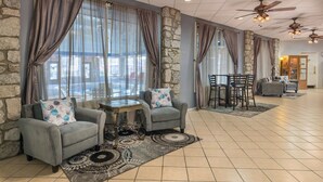 A spacious lobby with stone walls, large windows with curtains, a seating area with armchairs and a small table, and a ceiling fan. - 2BD Deluxe/Branson - w/Pools, Barbecue, Gym! (Branson)