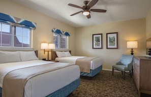 A hotel room with two beds, a ceiling fan, a chair, and framed pictures on the wall.