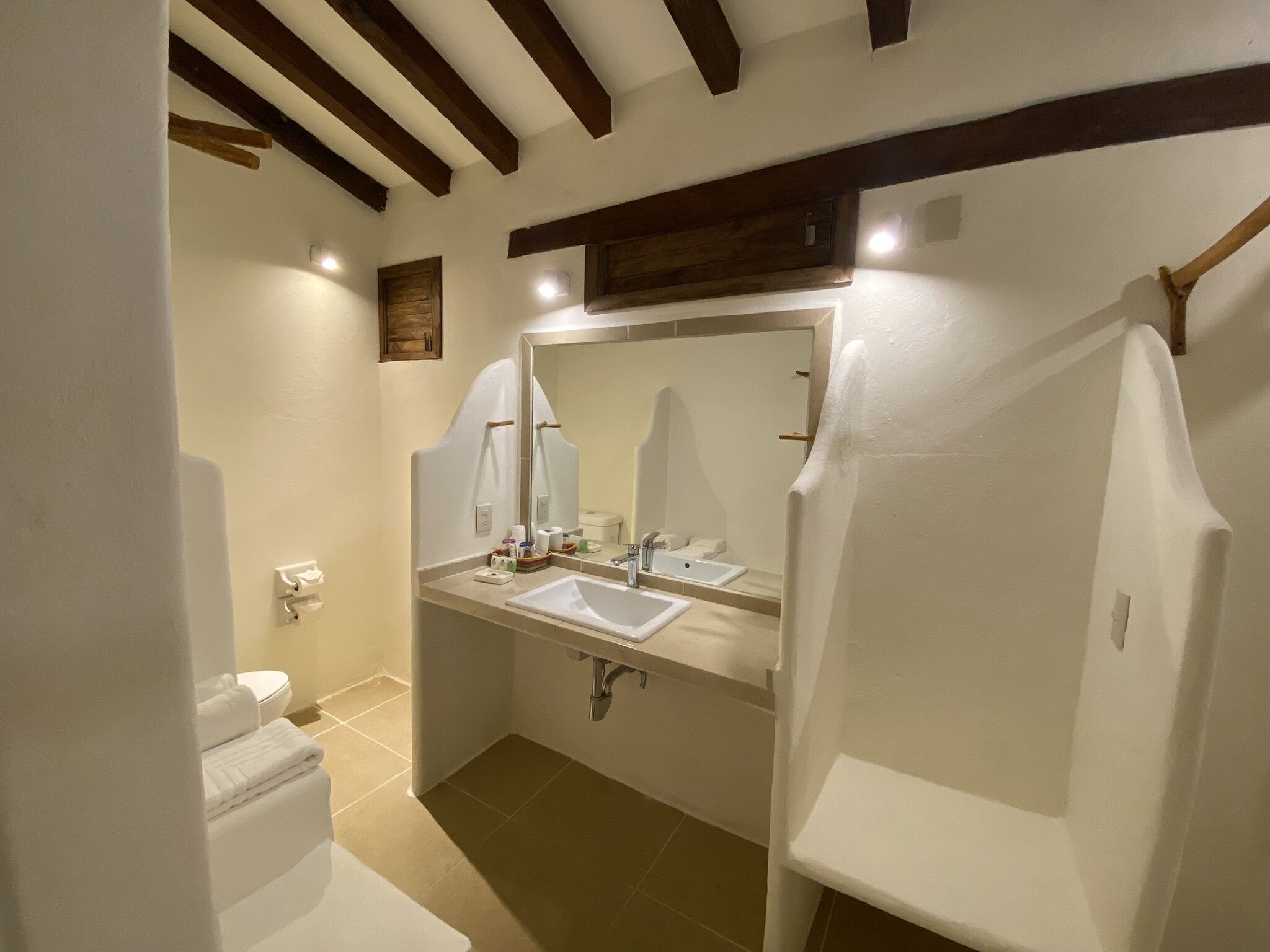 Une salle de bain avec des toilettes, deux lavabos, un grand miroir et des poutres en bois au plafond.