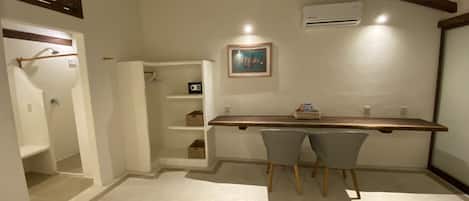 Een knus, klein kamertje met een houten plafond, een witte muur, een tafeltje met twee stoelen, een lijst met een afbeelding en een inbouwplank met opbergdozen.