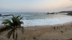 A beach with waves, palm trees, and people. - Casa Mandarina (Santa María Tonameca)