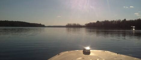 A boat on calm water with a clear sky and distant trees.