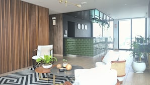 A modern lobby with a wooden wall, a green brick counter, and a seating area with white chairs and a round table. - LOFT LIMA -Depa- Magdalena del Mar (Lima)