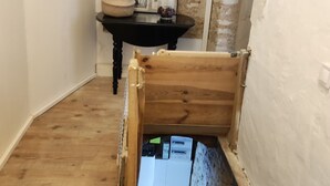 A room with exposed brick walls, a wooden floor, a small table with a picture frame, and a partially visible bed.