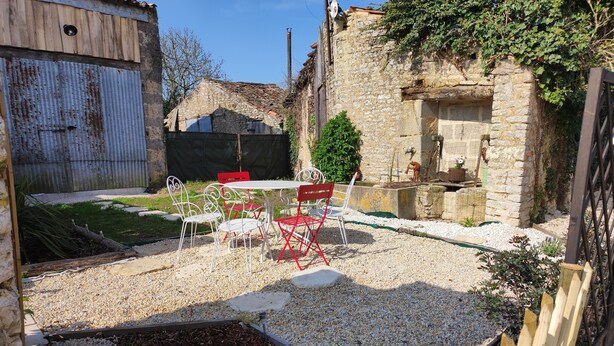 A rustic outdoor seating area with a gravel patio, stone walls, and a small garden.