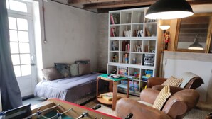 A cozy living room with a foosball table, a sofa, a bookshelf, and a window with curtains.
