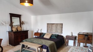 A bedroom with a bed, a wooden dresser, a nightstand, a desk, and a hanging lamp.