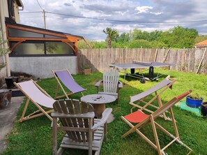 Un patio trasero con mesa de ping pong, una mesa redonda y varias sillas Adirondack.