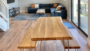 A spacious living room with a wooden table, a sectional sofa, and artwork on the wall. - Tree Top Retreat-Pool-Playground-Brewery (Dripping Springs)