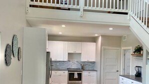 A spacious kitchen with a wooden table and benches, white cabinets, and a staircase leading to an upper level. - Tree Top Retreat-Pool-Playground-Brewery (Dripping Springs)