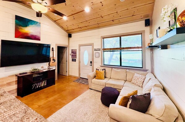 Una sala de estar acogedora con televisor, techo de madera y un ventanal grande.