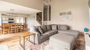 A spacious living area with a grey sectional sofa, a wooden dining table, and a staircase leading to an upper floor.