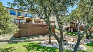 A residential area with a two-story house, a wooden fence, and a landscaped garden with trees and a stone pathway. - Parkview Retreat- Lake View • Fire Pit • Hot Tub (Canyon Lake)