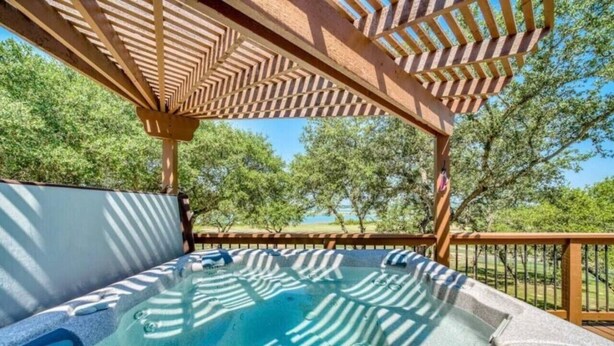 A hot tub under a wooden pergola with a view of trees and a body of water. - Parkview Retreat- Lake View • Fire Pit • Hot Tub (Canyon Lake)