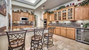 A kitchen with wooden cabinets, a marble countertop, and a central island with bar stools. - Parkview Retreat- Lake View • Fire Pit • Hot Tub (Canyon Lake)