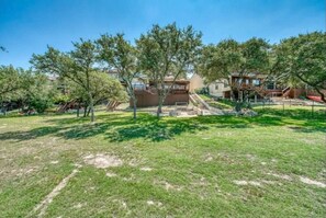 A residential area with a grassy lawn, trees, and a building with a staircase leading to a deck. - Parkview Retreat- Lake View • Fire Pit • Hot Tub (Canyon Lake)