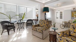 A spacious living area with a sofa, chairs, and a dining table. There are large windows providing natural light and a view outside. - Impeccable 4-bed House in São Domingos de Rana (Cascais)