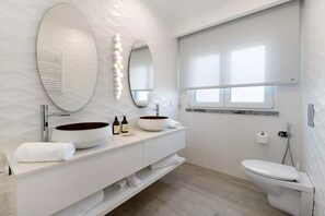 A modern bathroom with two oval mirrors, a large vessel sink, a toilet, and a window providing natural light. - Impeccable 4-bed House in São Domingos de Rana (Cascais)
