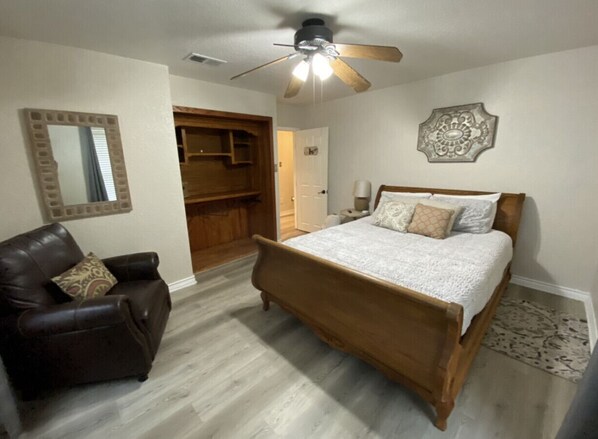 A bedroom with a wooden bed, a leather chair, a ceiling fan, and a walk-in closet.