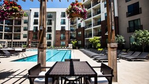 A poolside area with a rectangular pool, lounge chairs, and a pergola with hanging flower baskets.