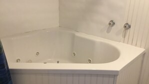 A white bathtub with four faucets, set against a white wall with vertical paneling. - Serenity Room located inside the Ivory Mansion
 (L'Anse)