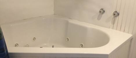A white bathtub with four faucets, set against a white wall with vertical paneling.