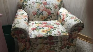 A floral-patterned armchair with a cushioned seat and backrest, positioned against a striped wallpaper background. - Serenity Room located inside the Ivory Mansion
 (L'Anse)