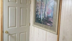 A white door with a gold handle and a framed painting of a forest scene. - Serenity Room located inside the Ivory Mansion
 (L'Anse)