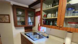 Cucina con mobili in legno, lavello in acciaio inossidabile e finestra con tenda rossa.