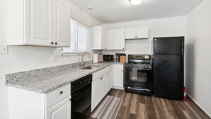 A kitchen with white cabinets, granite countertops, a black refrigerator, a stove, and a microwave.
