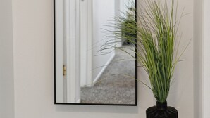 A hallway with a mirror reflecting a door and a plant on a wooden stool.