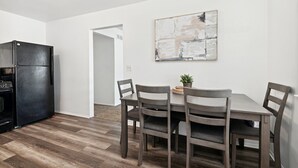 A dining area with a table and four chairs, a black refrigerator, and a painting on the wall.
