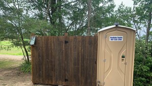 Eine mobile Toilette mit einem Schild, auf dem “VanDyke Sentic 607-535-2410” steht, und einem Holzzaun im Hintergrund.