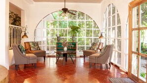 Une pièce spacieuse avec une grande fenêtre en arc de cercle, deux fauteuils, une petite table sur laquelle est posé un vase, et un ventilateur de plafond.