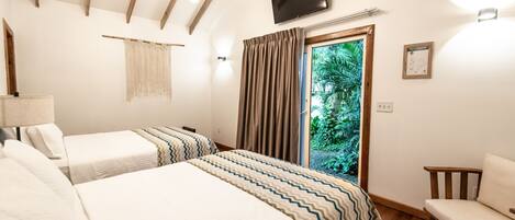 A hotel room with two beds, a TV, a wooden ceiling, a window with curtains, and a view of greenery outside.