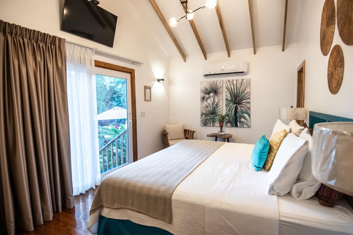 Ein Schlafzimmer mit Bett, Wandfernseher, Klimaanlage und einem Balkon mit Vorhängen.