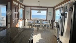 Una cocina con vista al mar, un comedor con sillas blancas y un refrigerador grande.