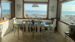 Un comedor con vista al océano, una mesa redonda con sillas y una lámpara colgante.