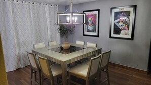A dining area with a rectangular table, six chairs, a vase, a chandelier, and two framed artworks on the wall.
