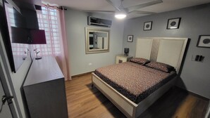 A bedroom with a bed, a desk, a mirror, and an air conditioning unit.