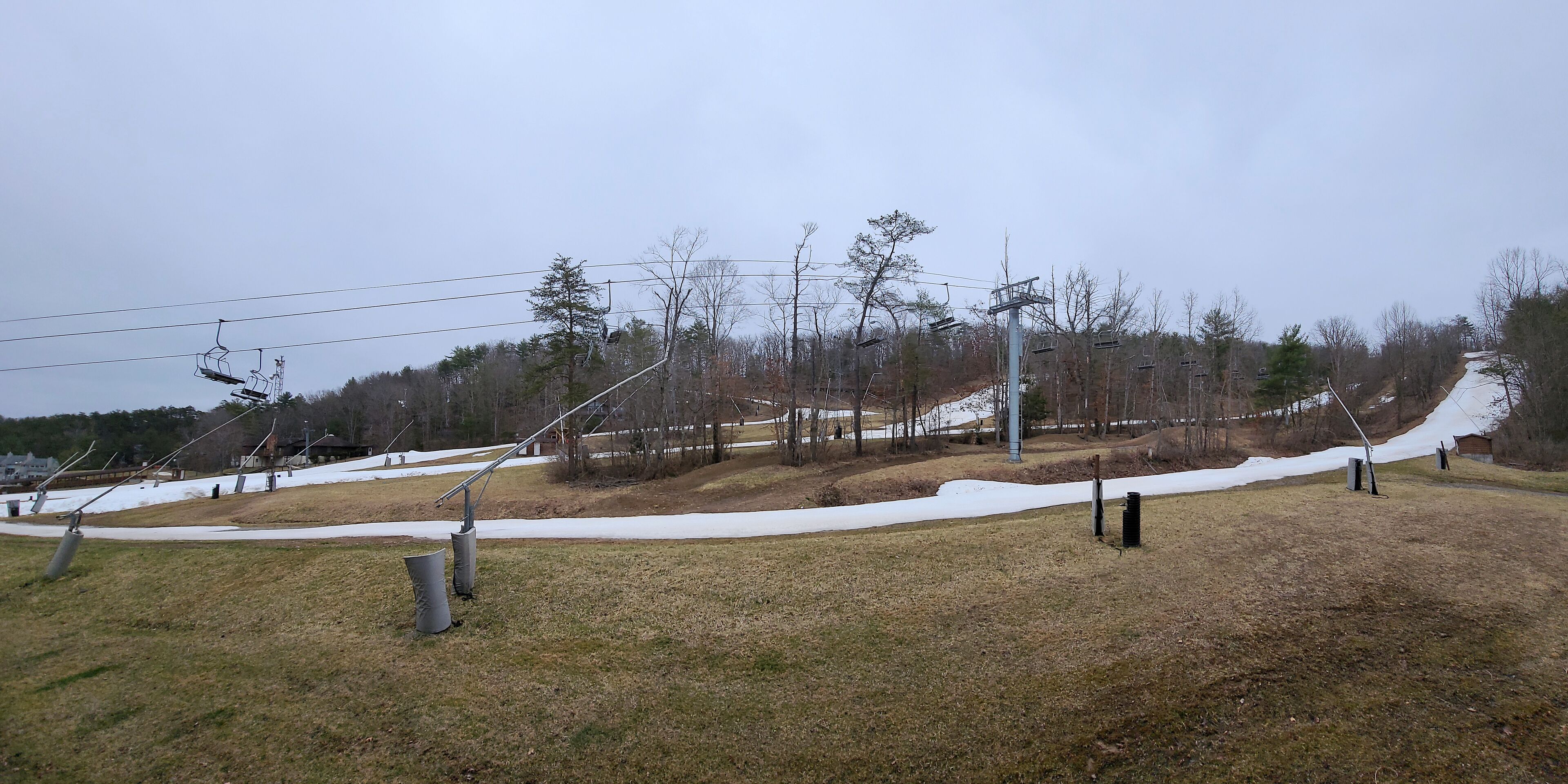 A ski lift area with chairs and cables, a snow-covered slope, and a grassy foreground.