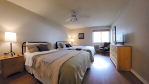 Une chambre avec deux lits, une commode, un bureau, un ventilateur de plafond et une fenêtre.
