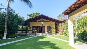 Una casa con techo de tejas, un porche y un jardín con césped y árboles.