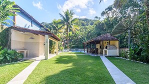 Un espacio exterior cuidado con piscina, zonas de estar cubiertas y abundante vegetación.