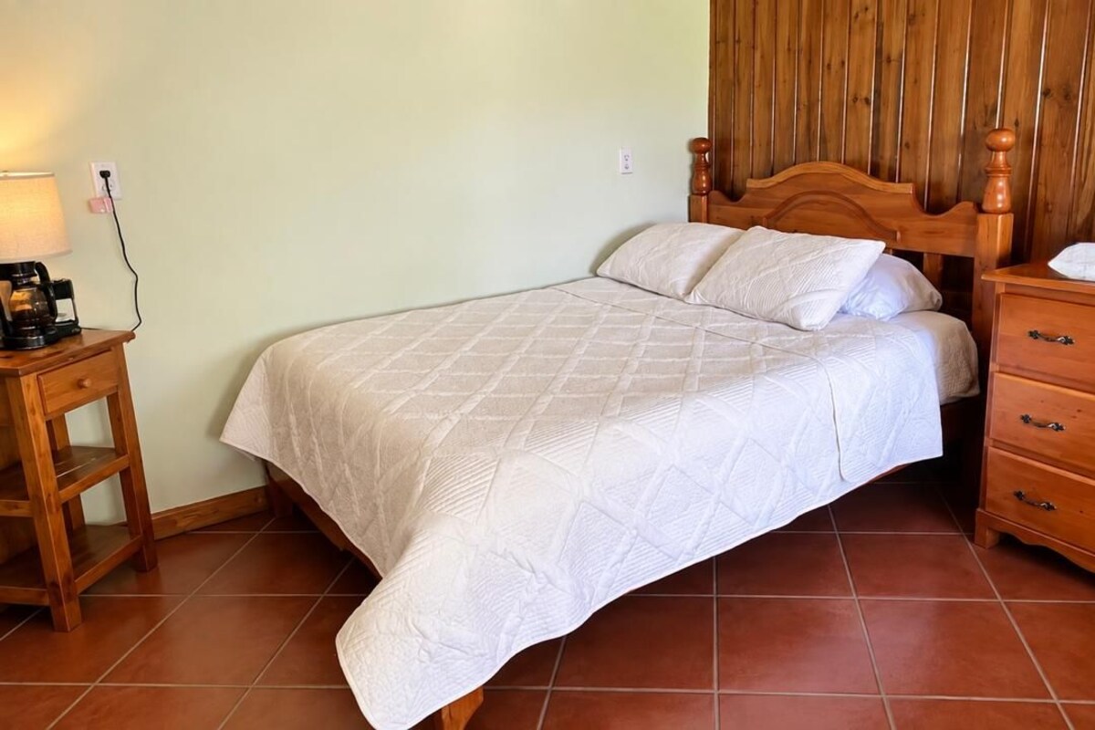 Un dormitorio con cama, cabecera de madera, mesita de noche, lámpara y cómoda.