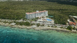 An aerial view of a hotel with multiple floors, a swimming pool, and a beachside location.