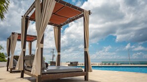A covered outdoor seating area with a pool in the background.