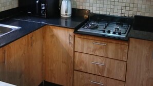 Una cocina con gabinetes de madera, una estufa a gas, un microondas y un hervidor.