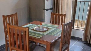 Un comedor con una mesa y sillas de madera, un refrigerador y vistas al exterior a través de una puerta de cristal.